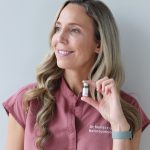 Dr. Marissa Gaucher, naturopathic doctor, smiling and holding a small vial of injectable treatment, wearing a clinic uniform against a neutral background.