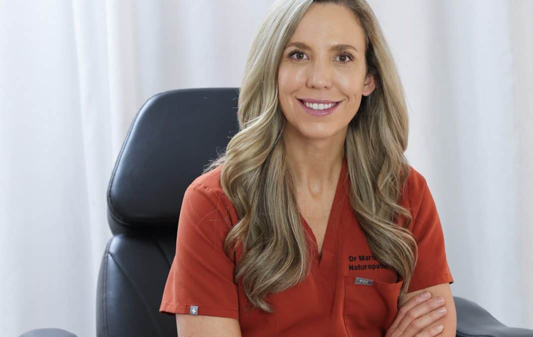 Dr. Marissa Gaucher, ND, seated in red scrubs at her clinic